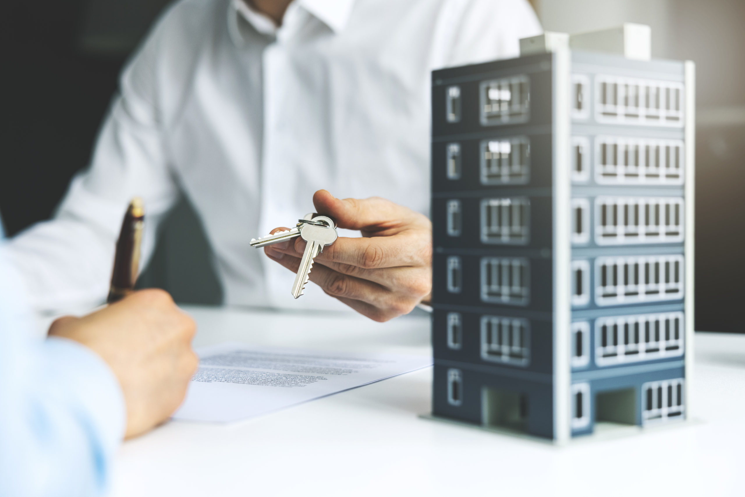 Tips For Choosing a Top Commercial Real Estate Agent. Commercial buyer signing apartment purchase mortgage agreement at real estate agent's office. Real estate agent is handing over the keys to the new property.